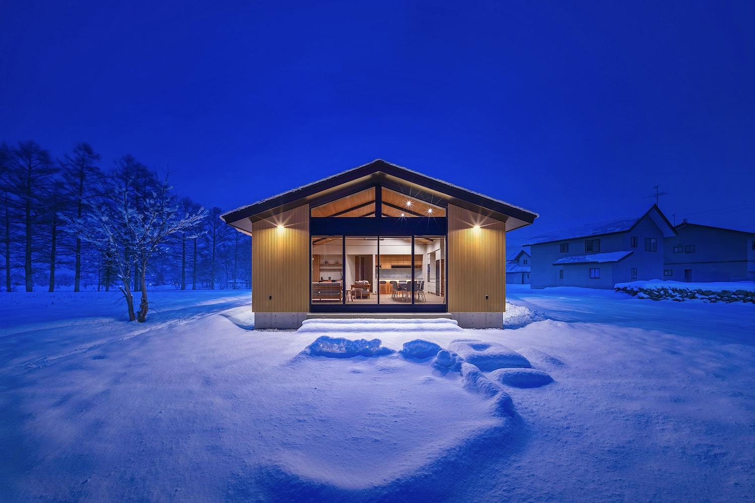 A warmly lit home centered in a snowy Hakuba landscape at dusk